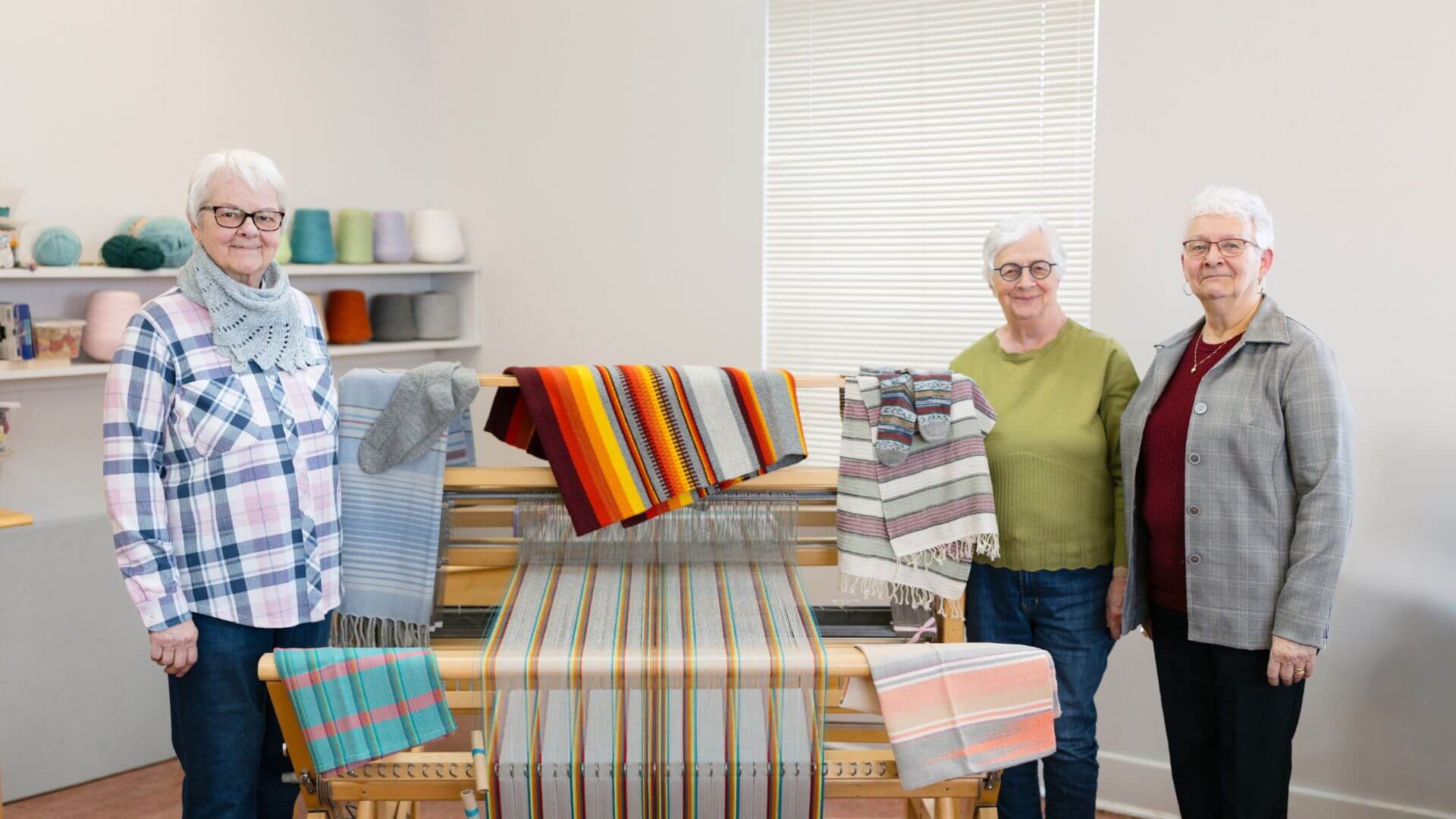 Trois membres du Cercle de Fermières Ville L’Islet présentent des créations textiles réalisées sur un métier à tisser.